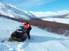 Stålis frees his snowmobile from deep snow on Varregaska, head of the lake behind